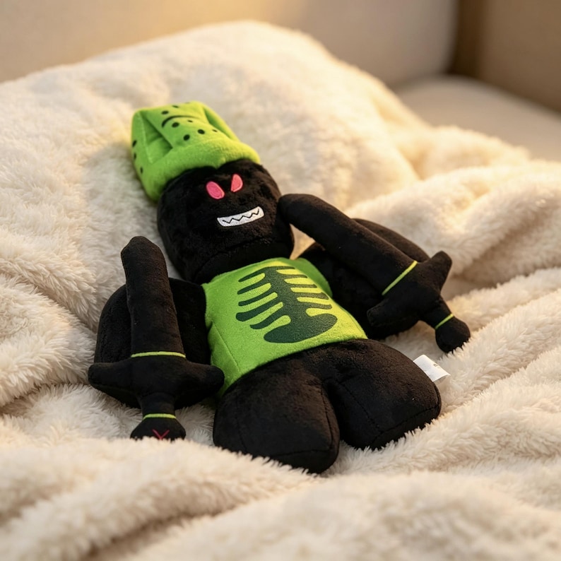 May include: A plush toy featuring a black character with a lime green hat and a matching lime green shirt displaying a dark green ribcage graphic. The character has red eyes, a white jagged mouth, and holds two black plush swords in its hands.