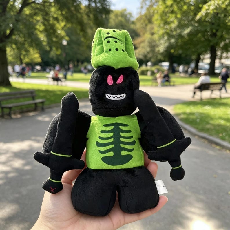 May include: A plush toy featuring a black character with a green helmet, a green torso with a dark green ribcage graphic, and two black swords. The character has pink eyes and a white mouth with sharp teeth, and is constructed from soft fabric.