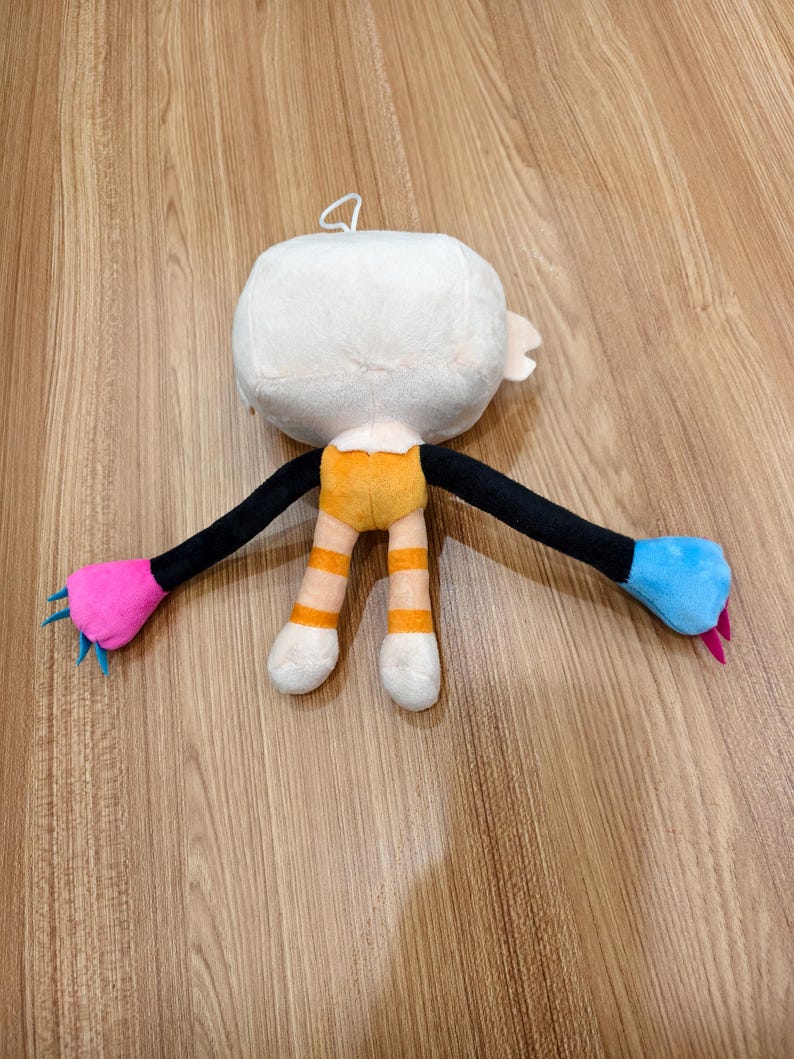 May include: A plush toy featuring a large white head, a yellow torso, and striped yellow and white legs. The long black arms end in one bright pink hand with blue claws and one bright blue hand with pink claws. A small white loop is on the head.