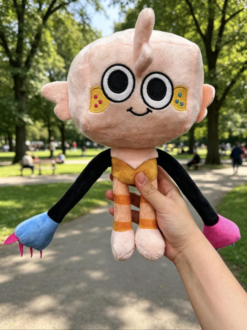 May include: A plush toy with a large, square, light pink head, black eyes, and a small smile. It features long black arms ending in one blue and one pink hand with small claws. The body is yellow and orange, with orange striped legs.