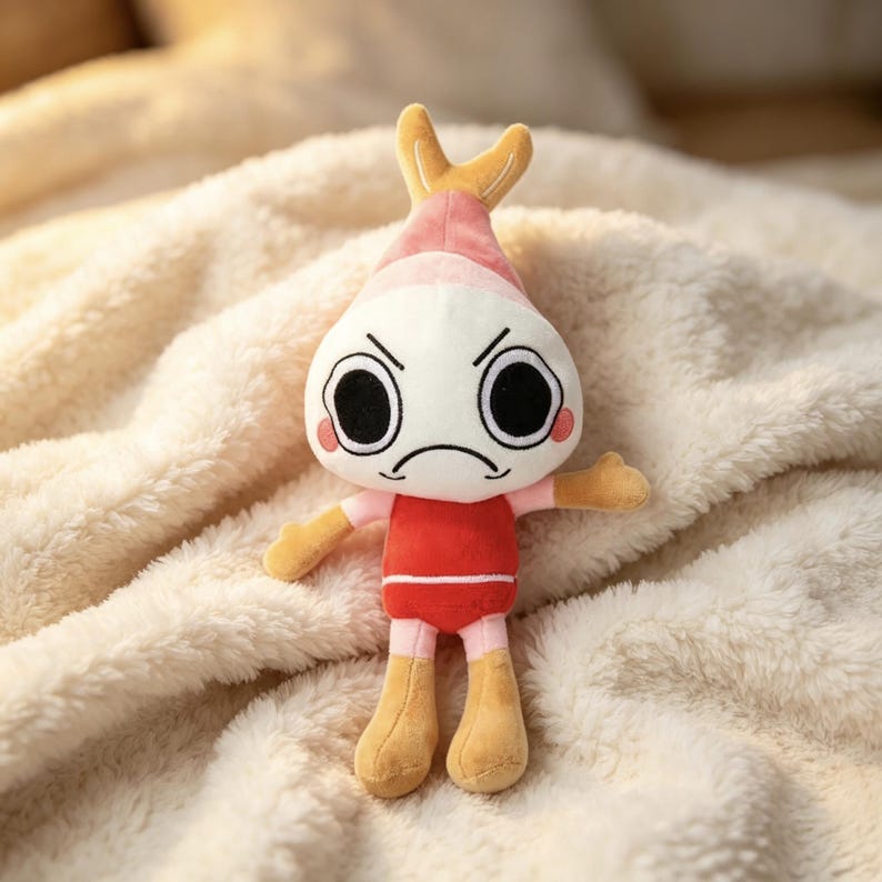 May include: A plush toy featuring a white, round head with large black eyes, a frowning mouth, and pink cheeks. It has a tan, pointed top, tan arms and legs, and a red torso. The character has a distinct, grumpy expression with angled eyebrows.