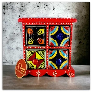 May include: A red wooden storage chest with four drawers featuring hand-painted ceramic fronts. The frame has white polka dots, and the drawers display colourful geometric and floral patterns in yellow, blue, orange, and black with round knobs.