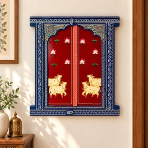 Könnte beinhalten: Ein rechteckiger Wand-Fensterrahmen aus Holz, bemalt in tiefem Blau mit komplizierten weißen Mustern. Die zwei zentralen roten Paneele zeigen handgemalte rosa Lotusblumen und cremefarbene Kühe als dekoratives Element.