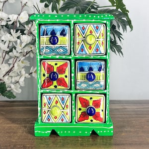 May include: A bright green wooden storage chest featuring six individual drawers. Each drawer front is decorated with unique, colorful hand-painted patterns in shades of blue, red, yellow, and white, finished with small, round, solid-colored knobs.