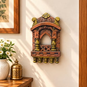 May include: A wall-mounted decorative piece shaped like an arched window frame with a textured finish in shades of terracotta, brown, and gold. The structure features a central pointed arch, two vertical pillars, and five small hanging finials.