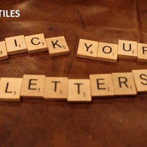 May include: Scrabble tiles spelling out the phrase "Pick your letters" on a brown leather surface. The tiles are arranged in a semi-circle shape.