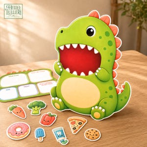 Könnte beinhalten: Ein grünes, dinosaurierförmiges Spielbrett mit weit geöffnetem Maul, begleitet von einer Essens-Sortiermatte mit Beschriftungen wie Main Food und Treat sowie verschiedenen kleinen, lebensmittelthematischen Ausschneidefiguren.