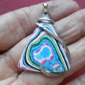 May include: A colorful triangular pendant with a swirling pattern of blue, green, pink, black, and white. The pendant is wrapped with silver wire and has a silver bail for a necklace chain. The pendant is held in a hand.
