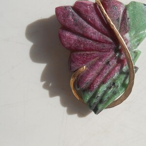 May include: A gold pendant featuring a carved green and pink gemstone in the shape of a flower. The pendant is attached to a gold chain.