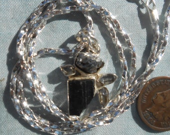 May include: A silver chain necklace with a pendant featuring a black tourmaline crystal surrounded by smaller clear crystals.