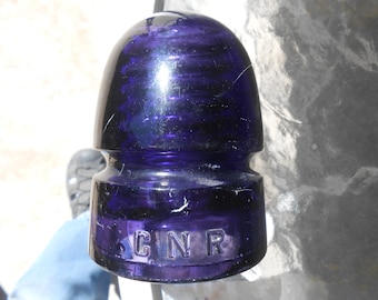 May include: A dark purple glass insulator with the letters "GNR" embossed on the bottom.