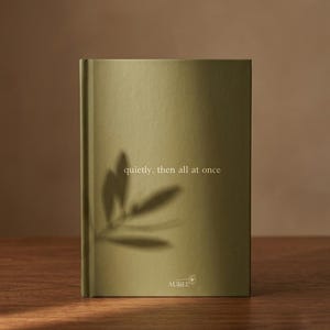 Pu&ograve; includere: Un libro rilegato con copertina verde oliva che riporta il testo "quietly, then all at once" stampato in bianco. La parte inferiore mostra il nome del marchio "AUREL" con una piccola icona a forma di fiore. L'ombra di una foglia &egrave; proiettata sulla copertina.