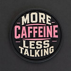 Könnte beinhalten: Ein kreisförmiger schwarzer Aufnäher mit erhabener Schrift in Creme und Pink. Der Text lautet MORE CAFFEINE in Creme und Pink, gefolgt von LESS TALKING in Creme. Das Design enthält horizontale Linien, die die Wörter trennen und ein grafisches Bild.