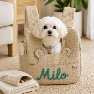 May include: A beige quilted pet carrier backpack featuring a small white dog inside. The front of the carrier displays the name Milo embroidered in teal script, two small fabric ears, and a side pocket containing a white bottle.