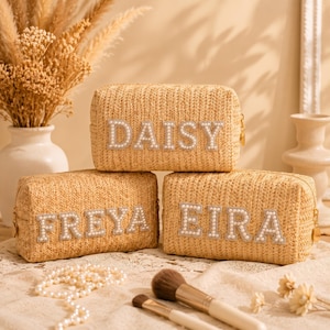 Può includere: Tre pochette rettangolari in paglia color beige chiaro. Ogni pochette presenta un nome composto da grandi lettere bianche decorate con perle sulla parte anteriore. I nomi sono DAISY, FREYA ed EIRA. Ogni pochette ha una cerniera color oro.