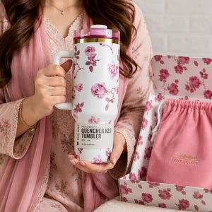 May include: White tumbler with a floral rose pattern, a pink lid, and a handle. The tumbler is labeled "QUENCHER H2.0 TUMBLER" and comes with a pink drawstring bag and a floral-patterned box. The tumbler is 40 oz / 1.18 L.