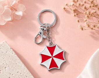Llavero metálico con forma de paraguas de Resident Evil, accesorio para videojuegos en rojo y blanco.