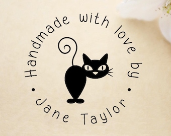 May include: A circular black ink stamp design featuring a stylized black cat with a curled tail in the center. The text "Handmade with love by Jane Taylor" is printed in a circular arrangement around the cat illustration on a light background.