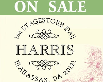 May include: A white and green sign with the text "ON SALE" in black lettering. Below the text is a black and white circular stamp with the text "1444 STAGESTONE WAY HARRIS MANASSAS, VA 20121". The stamp has a decorative design with two swirls.