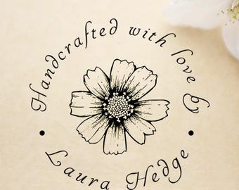 May include: A floral design with the text "Handcrafted with love by Laura Hedge" in a circular arrangement. The image features a detailed black and white flower illustration on a beige background, with a white flower in the upper right corner.