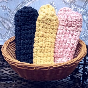 May include: Three crocheted pot holders in a wicker basket. The pot holders are black, yellow, and pink.