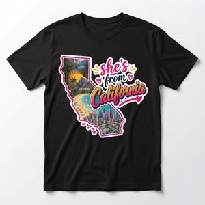 May include: A black t-shirt featuring a graphic of the state of California filled with a landscape illustration including palm trees, a mountain, a beach, and a city skyline. The text reads "she's from California" in pink and orange script.