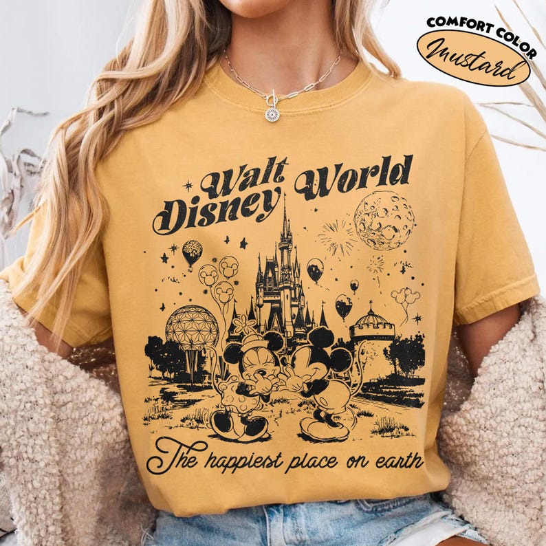 May include: Mustard-colored t-shirt with a black graphic of the Walt Disney World castle, Mickey and Minnie Mouse, and the text "Walt Disney World" and "The happiest place on earth". The shirt has a comfort color and a vintage design.