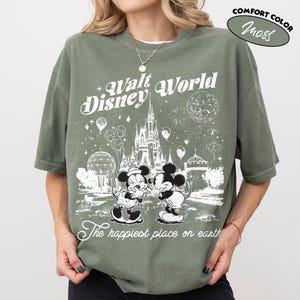 May include: Olive green t-shirt with a graphic of Mickey and Minnie Mouse in front of Cinderella's castle at Walt Disney World. The shirt has the text "Walt Disney World" and "The happiest place on earth."
