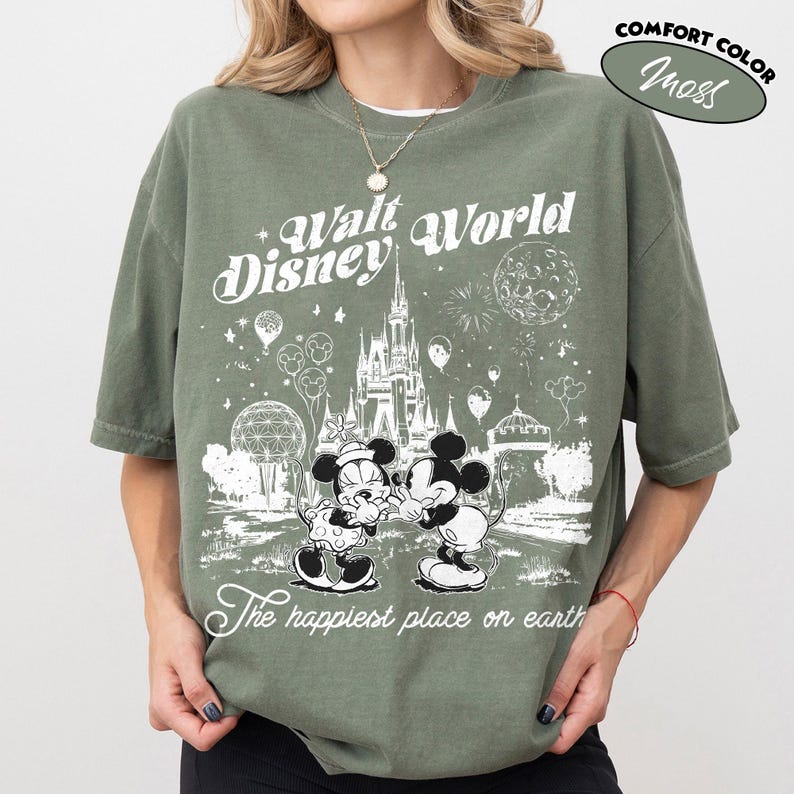 May include: Olive green t-shirt with a graphic of Mickey and Minnie Mouse in front of Cinderella's castle at Walt Disney World. The shirt has the text "Walt Disney World" and "The happiest place on earth."