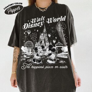 May include: Dark gray Comfort Colors t-shirt with a Walt Disney World graphic. The design features Mickey and Minnie Mouse, Cinderella's castle, and the phrase "The happiest place on earth."