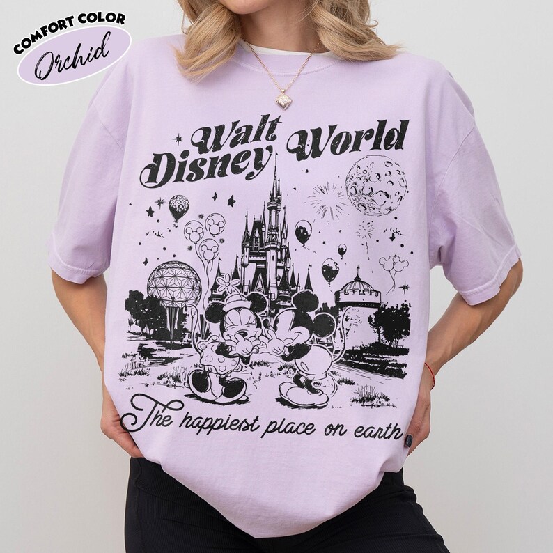 May include: A light purple t-shirt with a black graphic of Mickey and Minnie Mouse in front of a castle, with the text "Walt Disney World" and "The happiest place on earth". The shirt is labeled "Comfort Color Orchid".