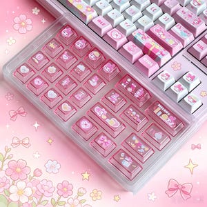 Pode incluir: Um teclado mecânico com teclas rosa claro e brancas com ilustrações de personagens, motivos florais e laços. Uma bandeja de plástico transparente contém teclas rosa translúcidas adicionais com gráficos impressos.