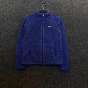 May include: A royal blue Patagonia fleece jacket featuring a high collar, a full-length front zipper, and two zippered side pockets. The garment is constructed with a textured, fuzzy fleece material and includes a small Patagonia brand logo patch on the upper left chest area.