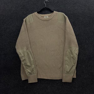 May include: A beige ribbed crewneck jumper featuring tonal fabric patches on the shoulders and elbows. The garment has a round neckline with a ribbed collar and cuffs, and a small L.L.Bean brand label is visible on the interior neck area.