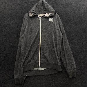 May include: A charcoal gray heathered zip-up hoodie featuring a white front zipper, a hood with a light gray interior lining, and a white DC logo printed on the upper left chest. The garment includes long sleeves with ribbed cuffs and a ribbed hem.