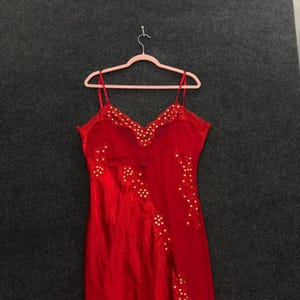 May include: A vibrant red slip dress featuring delicate spaghetti straps and a V-neckline. The garment is adorned with intricate lace detailing along the neckline and a diagonal floral lace pattern that extends down the front of the fabric.