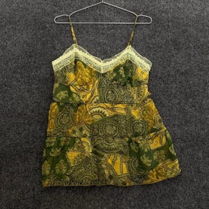 May include: A green and yellow paisley print camisole top with spaghetti straps and a lace trim neckline. The top is hanging on a metal hanger against a gray background.
