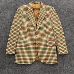 May include: A blazer with a brown, green, and white checkered pattern. The jacket has a notched lapel, two front pockets, and a single-button closure. The interior lining is a solid brown color.