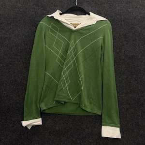 Könnte beinhalten: Grüner Langarmpullover mit weißem Rautenmuster und einem weißen Hemd mit Kragen darunter. Der Pullover hat einen V-Ausschnitt und weiße Manschetten. Der Hemdkragen ist am Ausschnitt sichtbar.