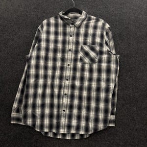 May include: A long-sleeve button-down shirt featuring a black and white plaid pattern with a gradient ombre effect. The shirt includes a standard collar, a single chest pocket on the left side, and a full-length front button closure with dark buttons.