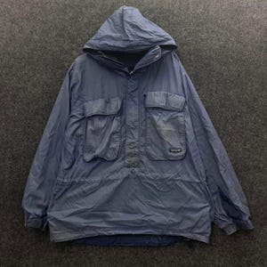 Puede incluir: Una chaqueta tipo pullover con capucha en color azul pizarra, con cierre de media cremallera, capucha con cordón y dos grandes bolsillos rectangulares en el pecho con solapa. Incluye una pequeña etiqueta de marca en el bolsillo derecho.