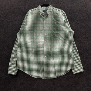 May include: A long-sleeve button-down shirt featuring a green and white gingham check pattern. The shirt includes a buttoned collar, a front button placket, and a small purple embroidered logo on the left chest area above the pocket.