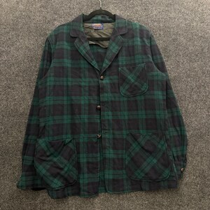 May include: A long-sleeve button-up jacket featuring a dark green and black plaid pattern. The jacket includes a notched lapel collar, one chest pocket, and two large lower patch pockets. It has three front buttons and a dark olive interior lining.