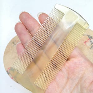 以下が含まれることがあります： 半透明の淡い黄色のヘアコーム。滑らかでしっかりとした中央の背骨で分けられた、2つの異なる細かい歯のセクションが特徴です。コームは上端が湾曲しており、下端はわずかにアーチ状で、全体的に滑らかで磨かれた仕上がりになっています。