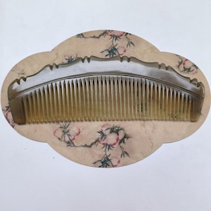 May include: A curved hair comb made of translucent, light brown horn material. The comb features a series of fine, evenly spaced teeth and a decorative, scalloped top edge. The material displays natural variations in color and semi-transparency.