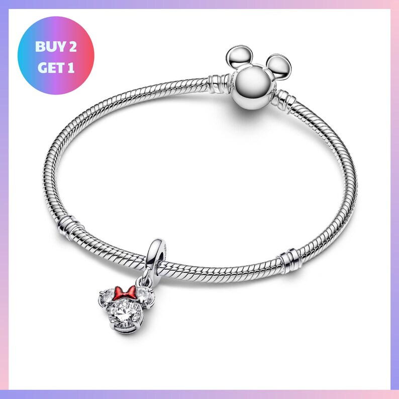 A silver bracelet with a charm featuring a red bow and a charm resembling a pair of ears, along with a tag that says "BUY 2 GET 1".