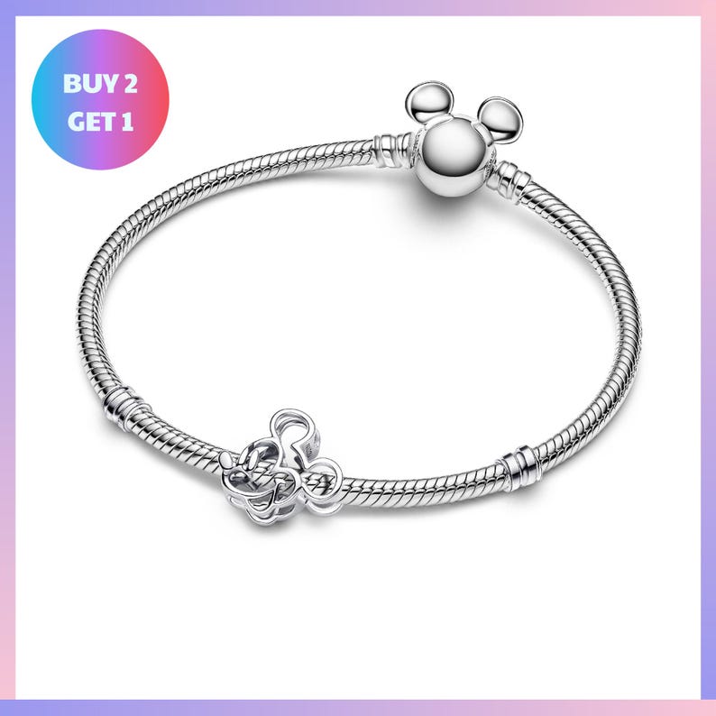 A silver bracelet with a charm and a tag, along with a circular sign that says "BUY 2 GET 1".