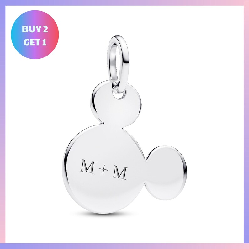 A silver charm in the shape of a Mickey Mouse, with the letters "M+M" engraved on it.