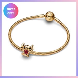 A gold-colored charm bracelet with a small, cartoon-like character on it, and a text overlay that says "BUY 2 GET 1".
