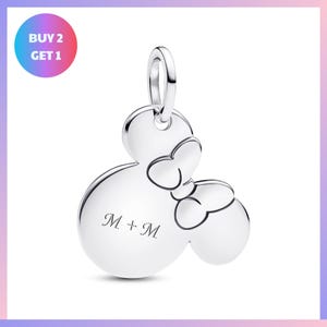 A silver charm in the shape of a Mickey Mouse with a bow tie, and the text "M + M" engraved on it.